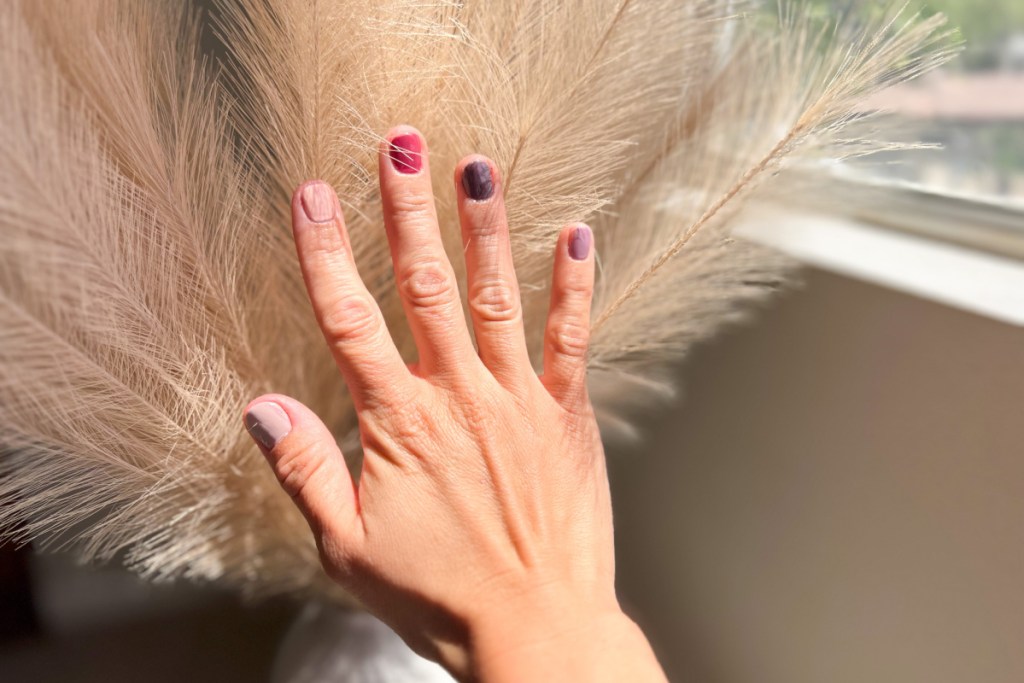 hand with multi colored pink nails in front of straw