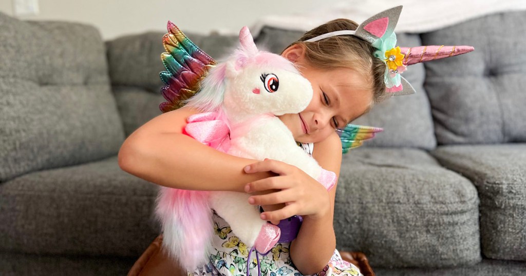 girl holding white unicorn toy with rainbow unicorn headband on