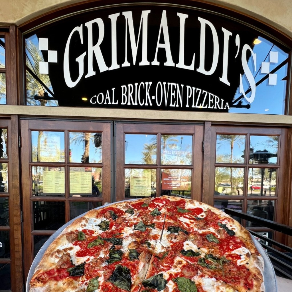 holding a whole pizza in front of Grimaldi's entrance