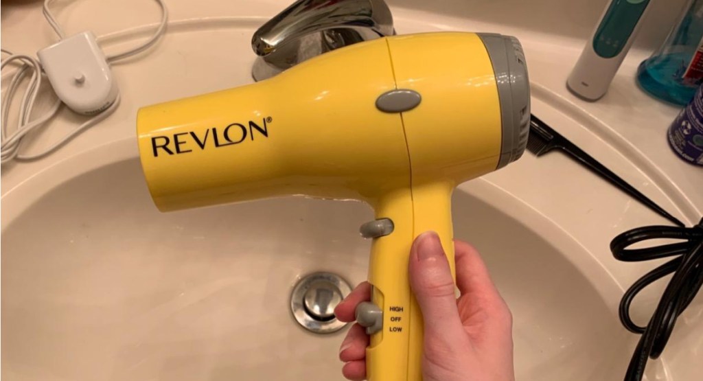 hand holding compact hair dryer in yellow in her bathroom