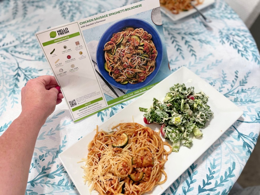 hello fresh recipe card in-hand behind a plate of pasta and salad