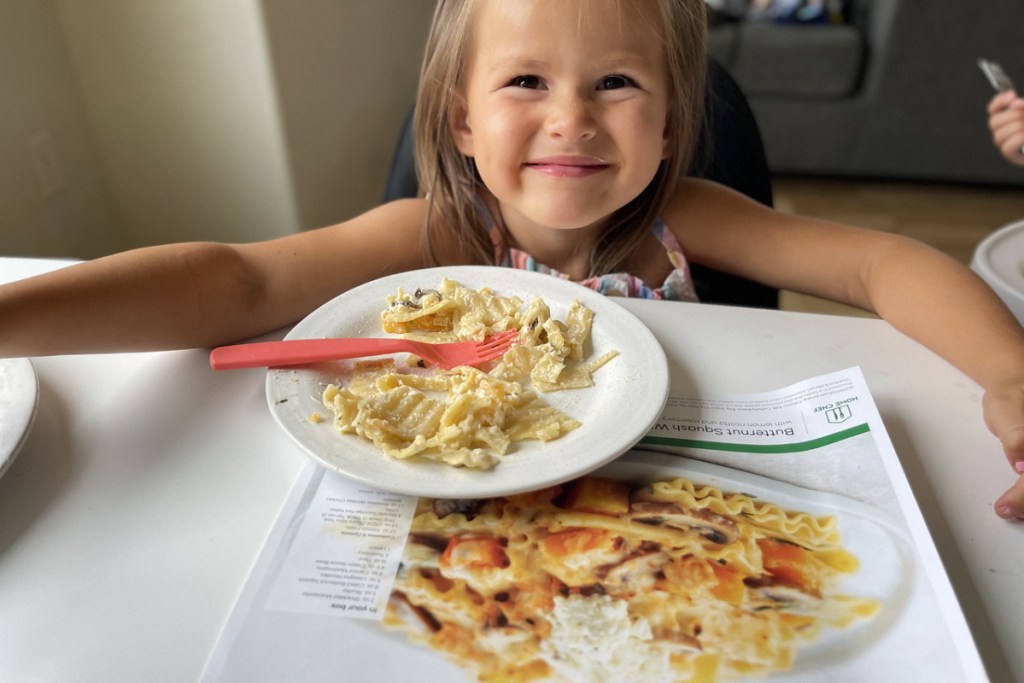 little girl in front of a plate of food and a home chef recipe card