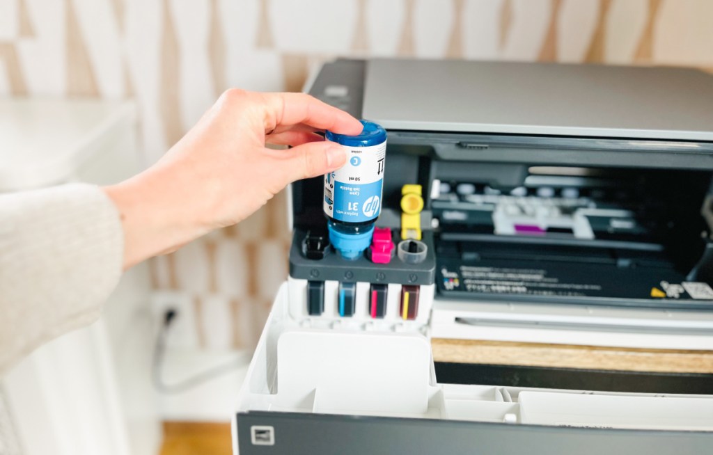 hand holding a bottle of ink and refilling an hp printer tank