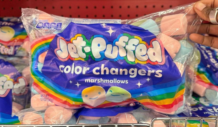 a womans hand grabbing a bag of jet puff color changers marshmallows from a store shelf