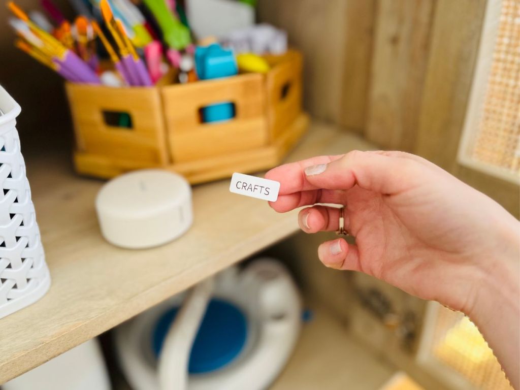 person holding "crafts" label with craft supplies and label maker in background