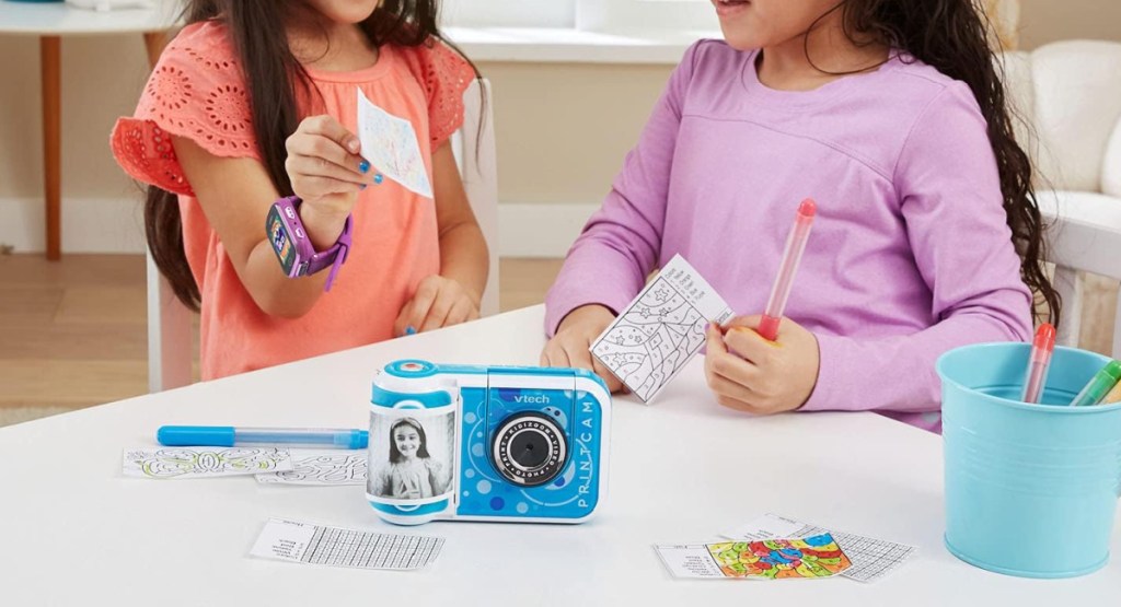 little girls plying with the digital camera for kids that also has printing on the table