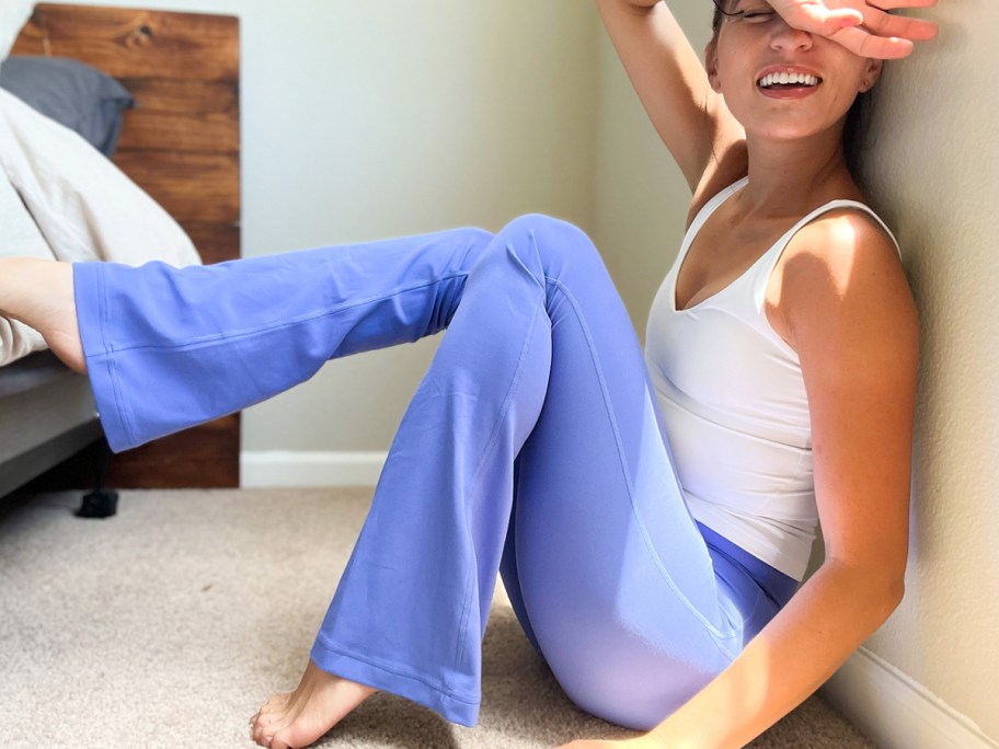 woman sitting on floor wearing purple flare pants and white tank top