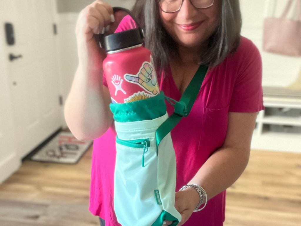 person putting pink water bottle in green crossbody water bottle bag 