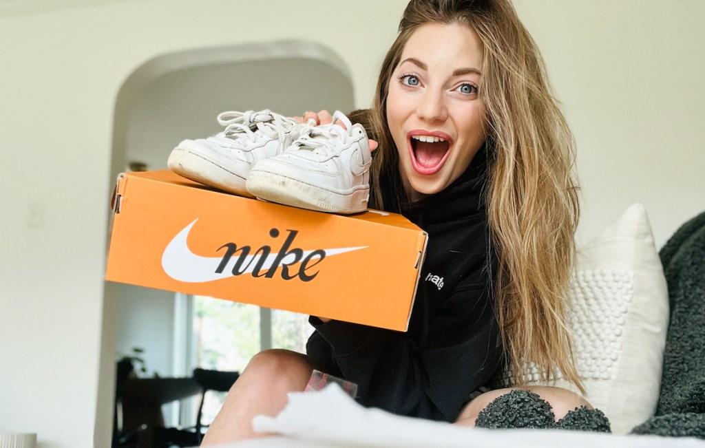 woman holding orange nike shoe box with white air force ones on top