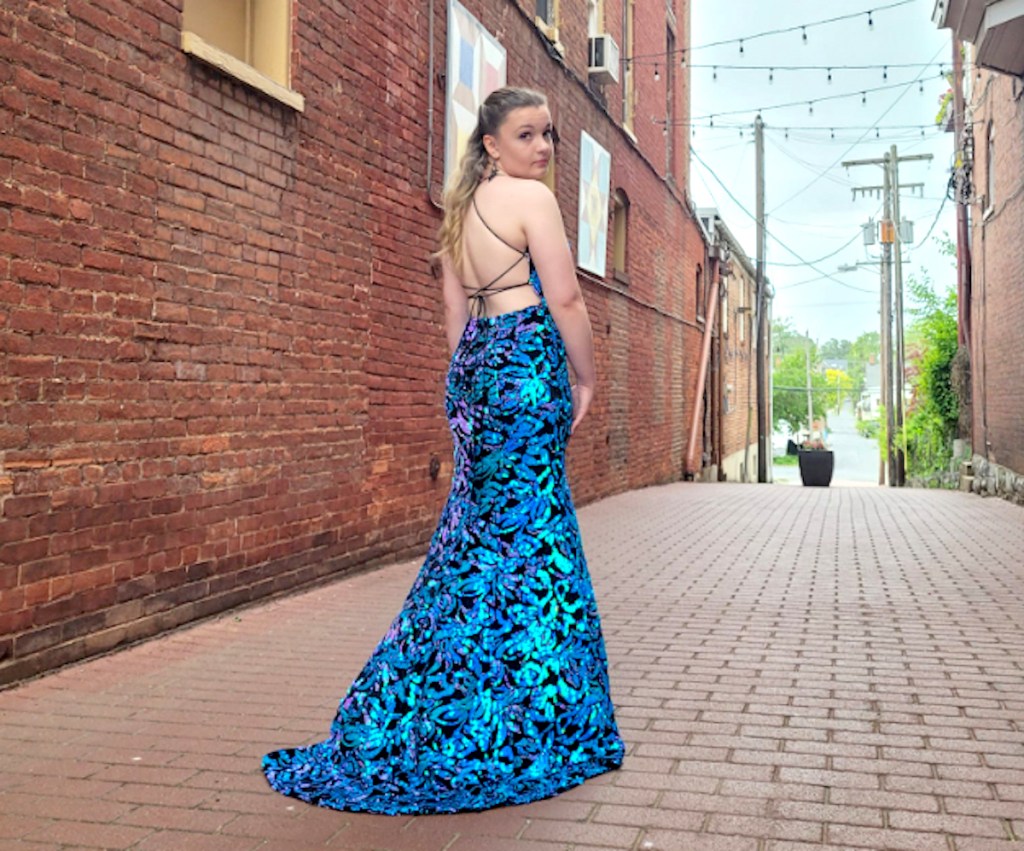 girl posing in blue shiny gown on brick sidewalk