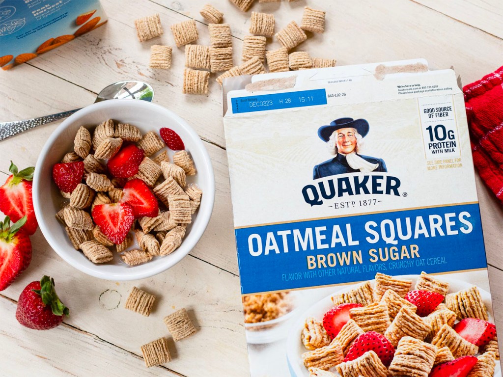 quaker oatmeal squares cereal box next to bowl of cereal with strawberries