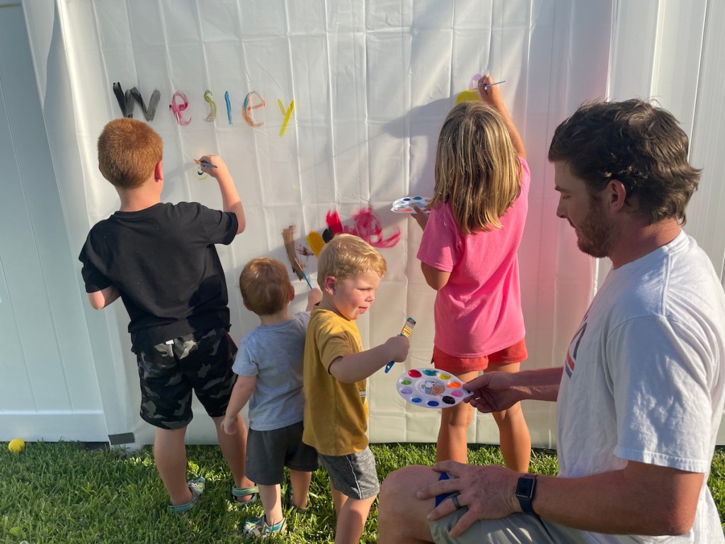 kids painting on shower curtain draped over white fence