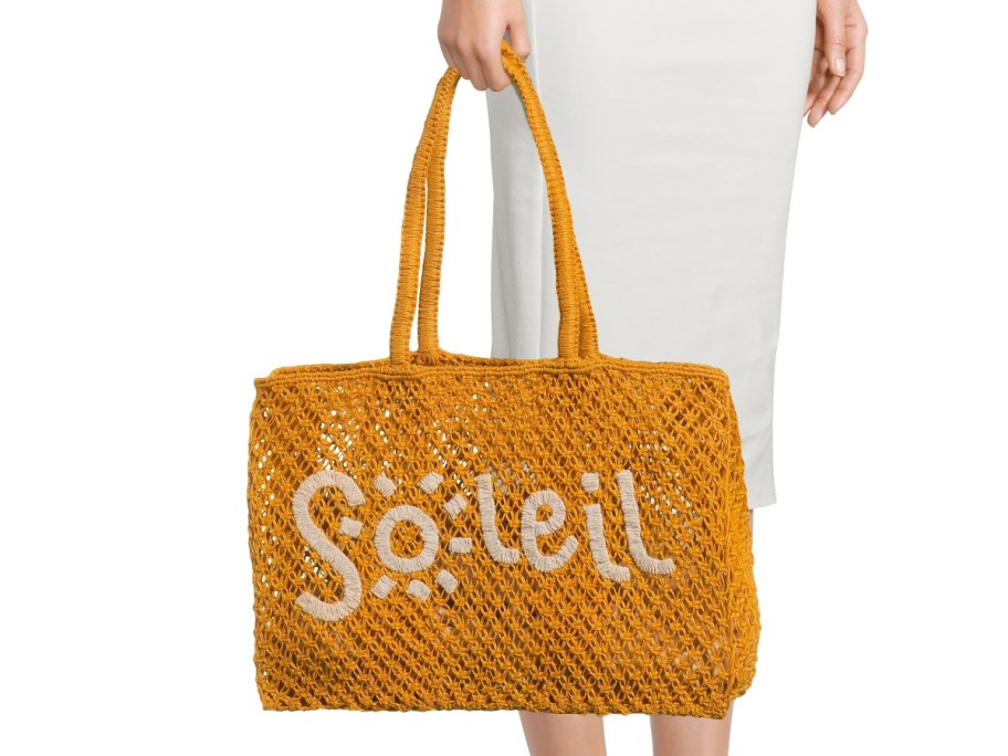 holding a yellow beach bag with the word Soleil on it