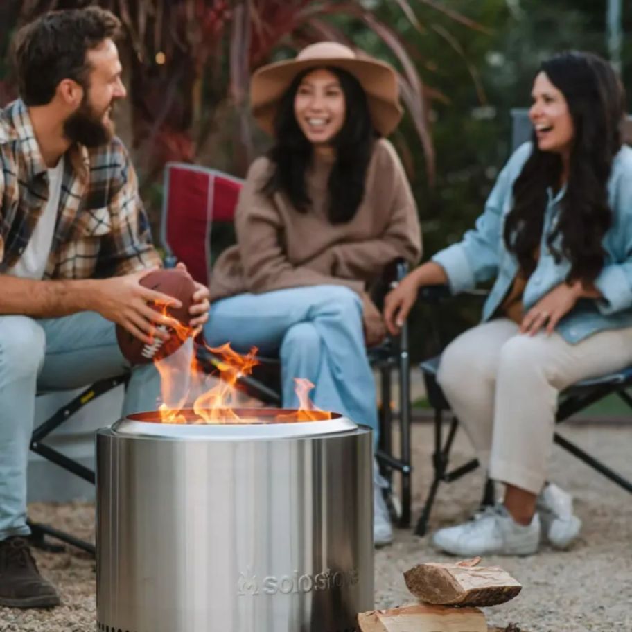 3 people sitting aorund a stainless steel solo bonfire stove
