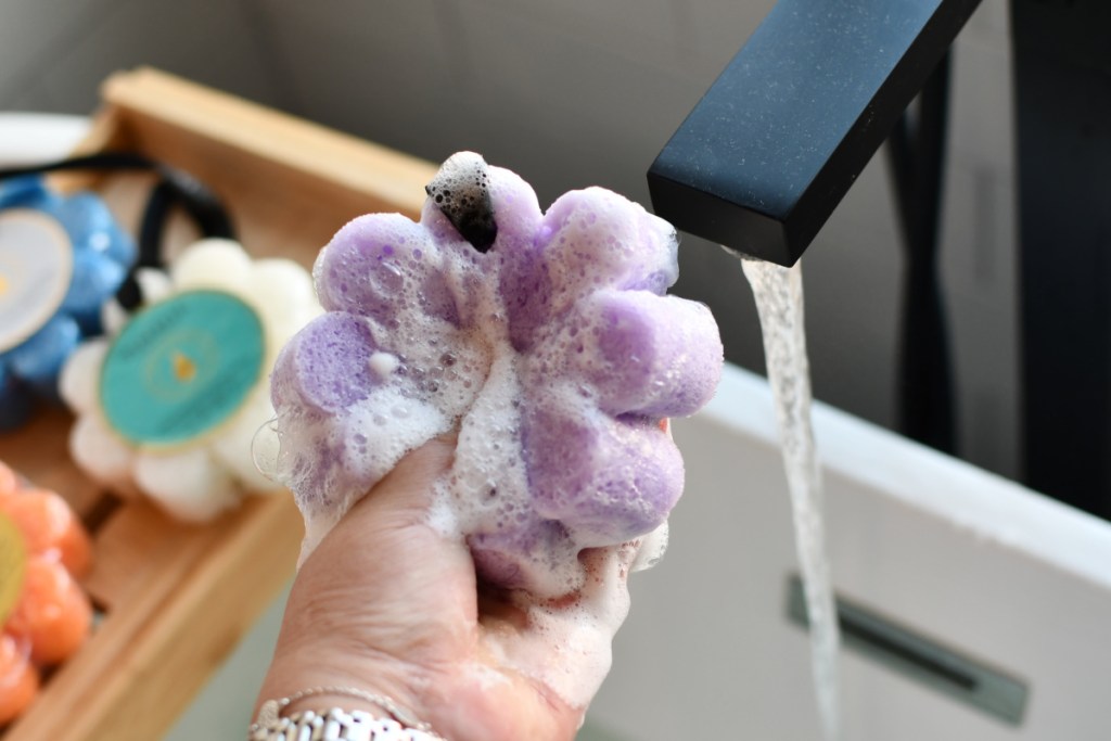 hand squeezing soap out of purple flower buffer
