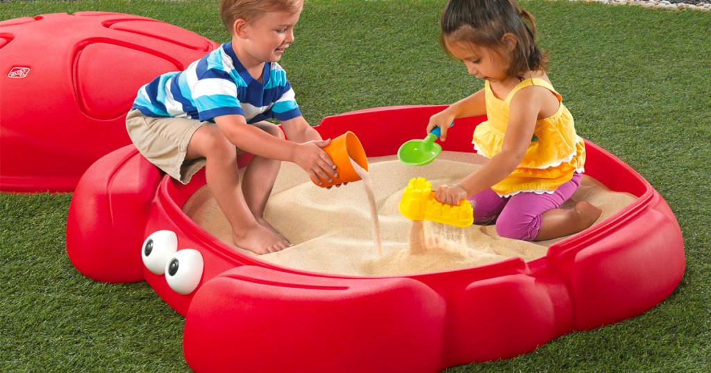 two children playing in red crab sandbox on grass