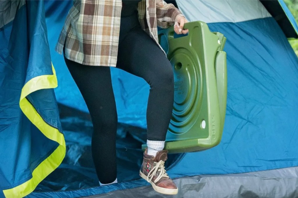 woman carrying green flip seat out of tent