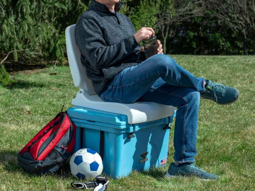 man sitting on flip seat on top of cooler at park