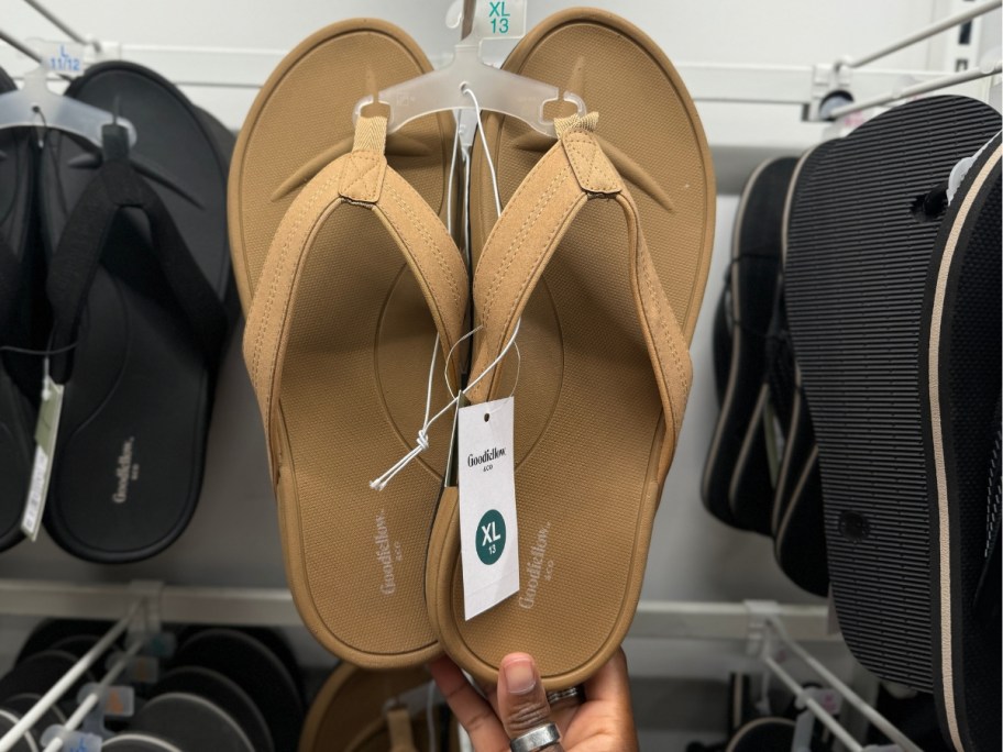 hand reaching for a tan pair of men's flip flop sandals on a display