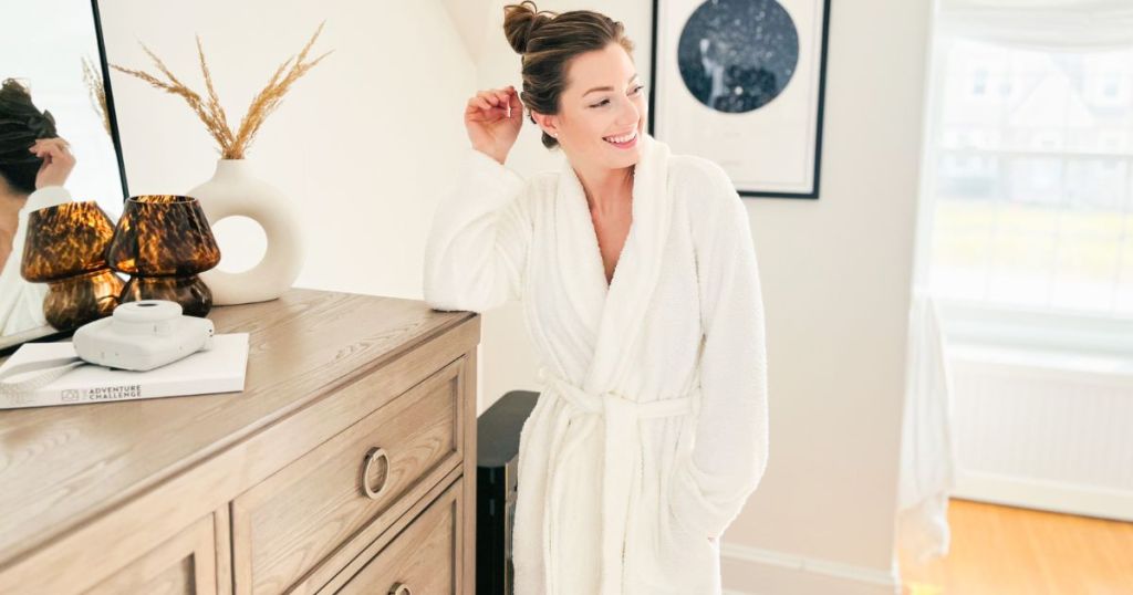 woman standing in plush white robe by dresser