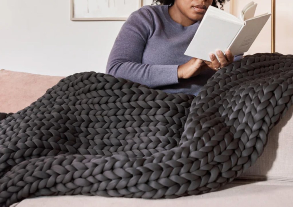 woman reading under large chunky knit blanket