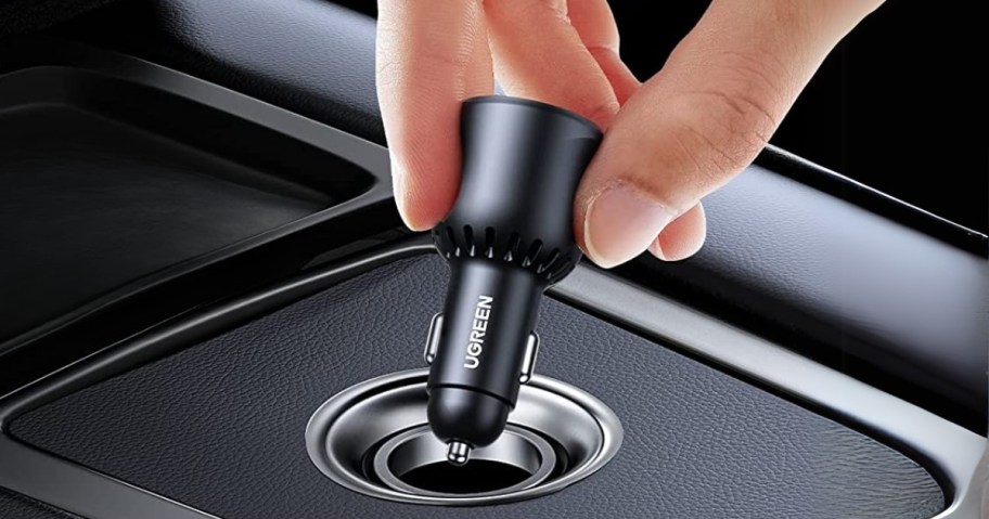 hand plugging a black UGREEN car charger into the port in a car