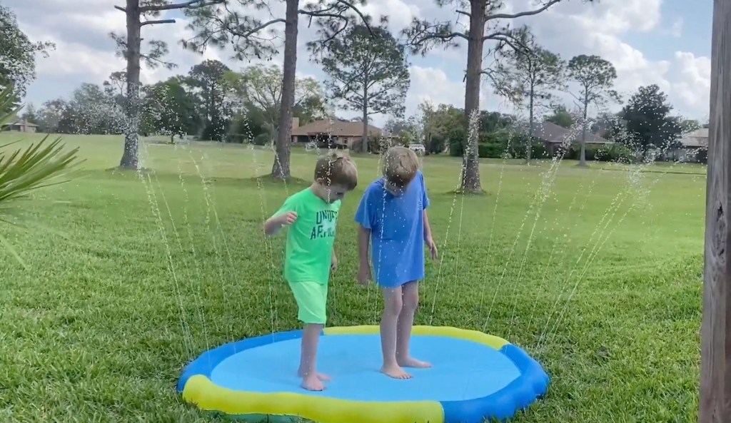 two boys playing in blue and green splash pad outside in grass