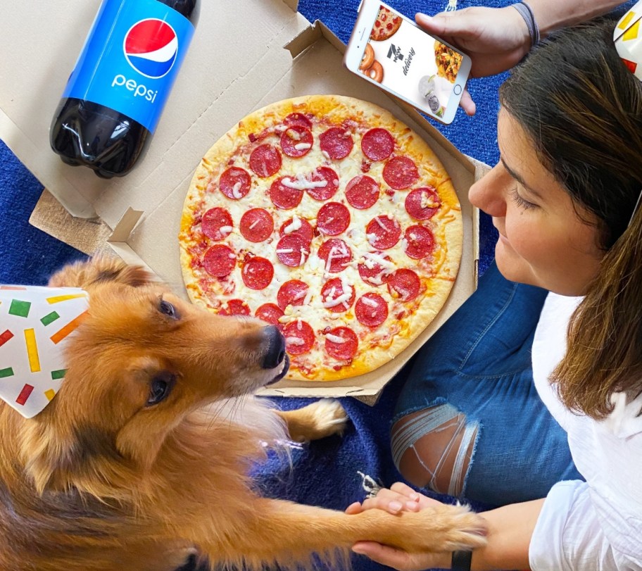 Woman holding a dogs paw next to a pizza box