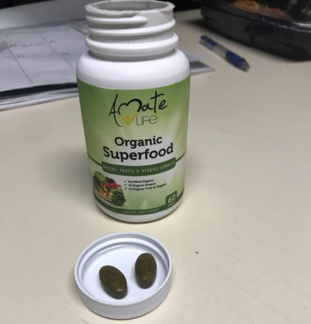 Amate Life Organic Superfood bottle with the cap off and two tablets in the cap