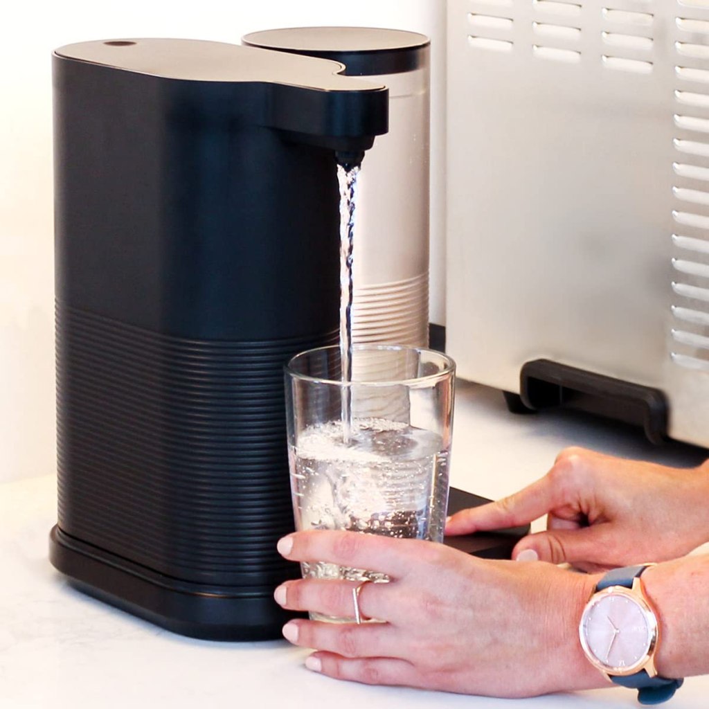 Hands holding a glass next to a water dispenser