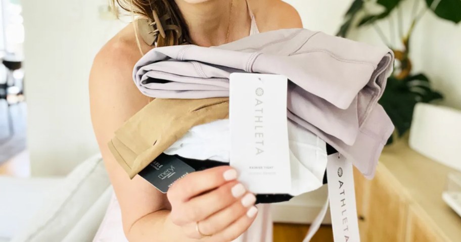woman holding athleta tag from a stack of folded clothes