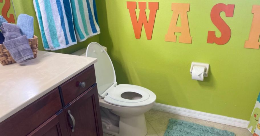 toilet with dual seat in bathroom next to green wall