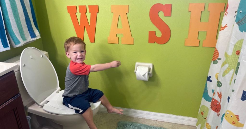 toddler sitting on toilet with toddler seat attached in bathroom