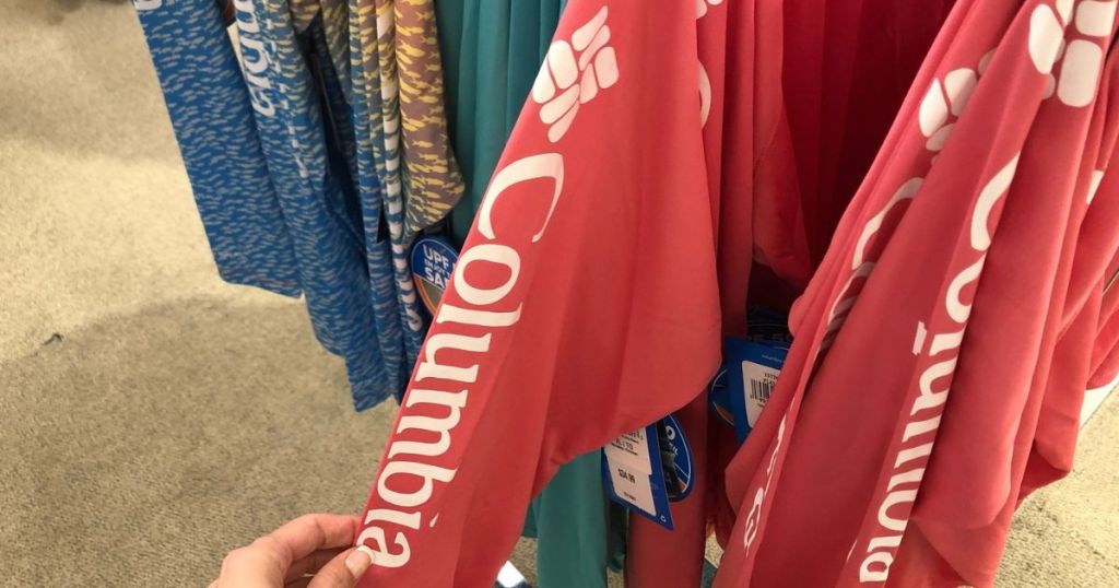 Hand pulling the sleeve of a Columbia shirt from a rack of shirts