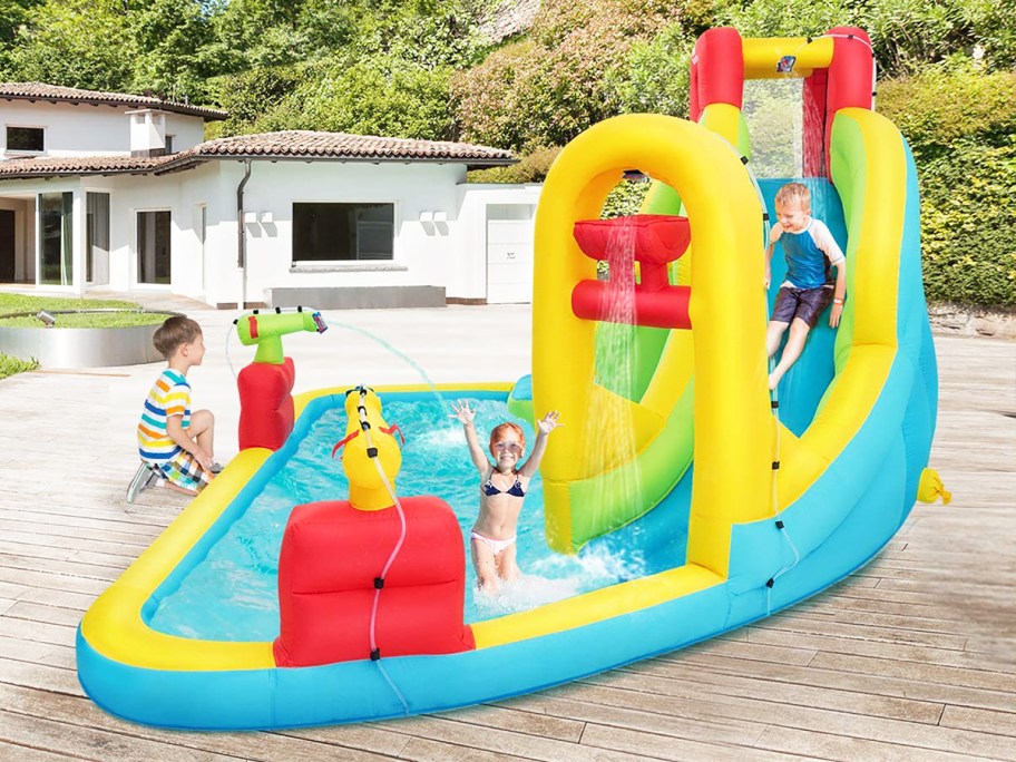 three kids playing on giant inflatable water slide in yard