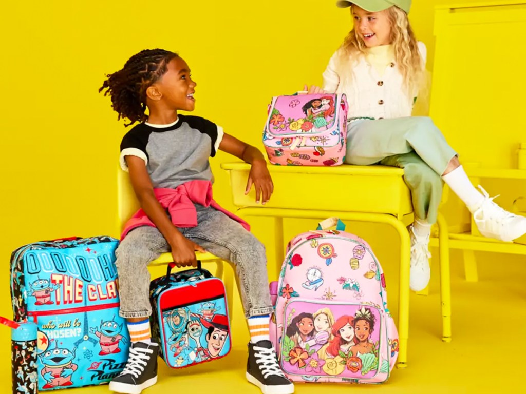 boy and girl sitting on yellow desk with disney backpacks and lunchboxes