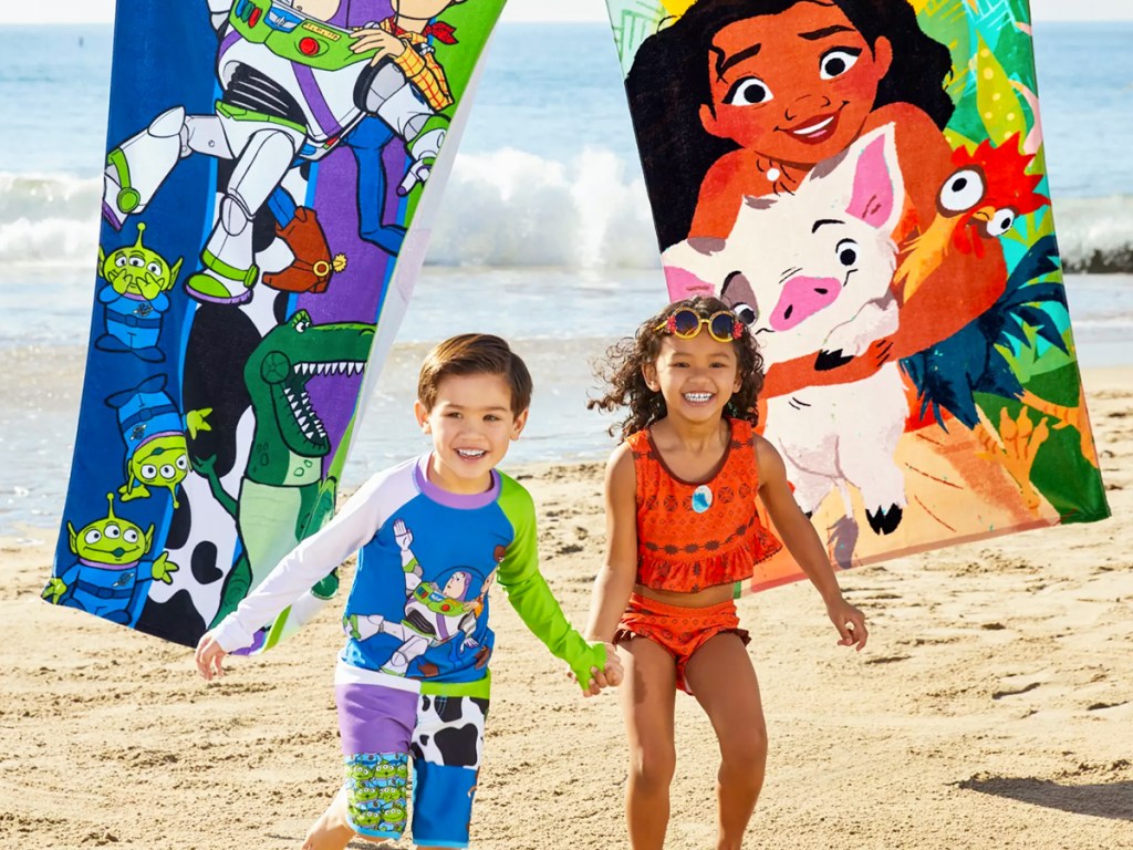two kids running on beach with dinsey beach towels behind him