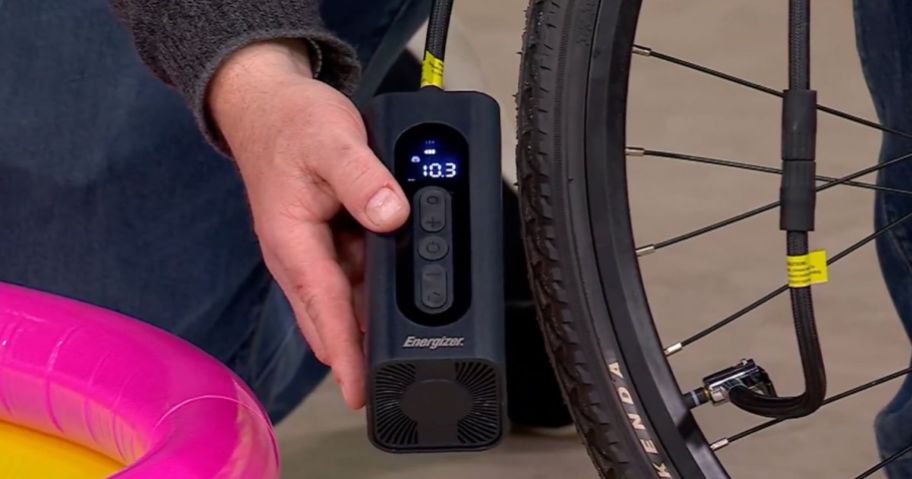Hand holding an Energizer Portable Compressor next to a bike tire