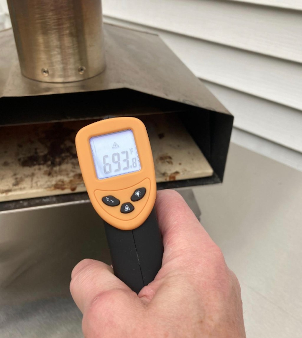 hand holding infrared thermometer in front of pizza oven