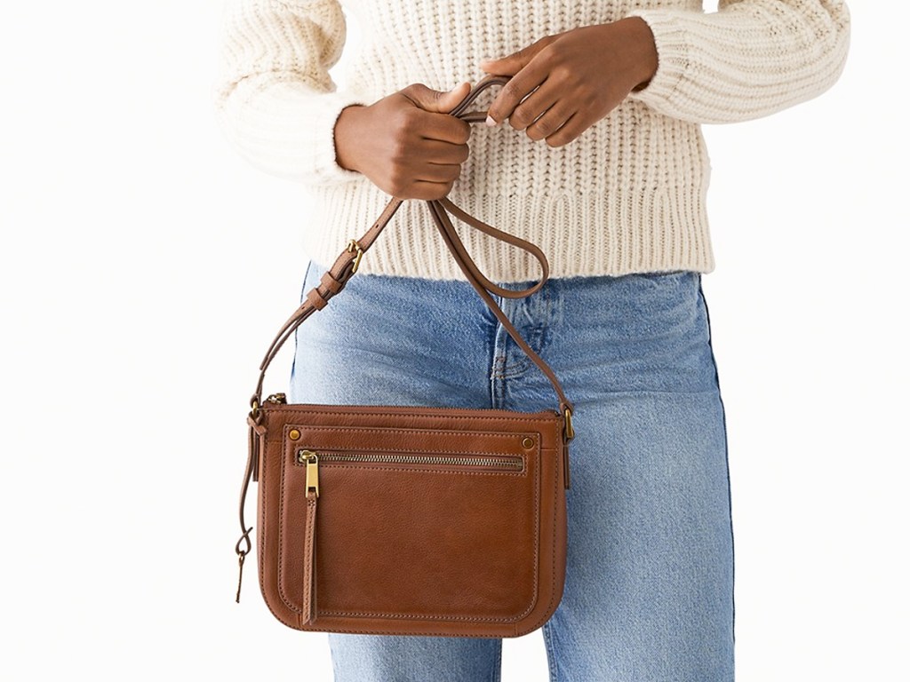woman in jeans and white sweater holding a brown crossbody bag