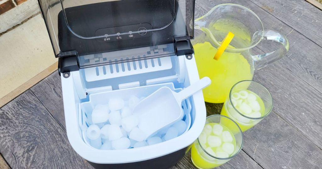 Free Village Ice Maker Filled with ice next to pitcher of lemonade and two glasses filled with ice and lemonade