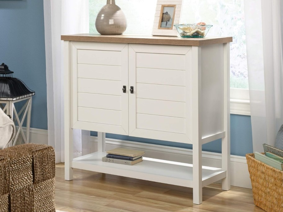 cabinet / sideboard / accent storage table in white with a light wood top sitting by a window