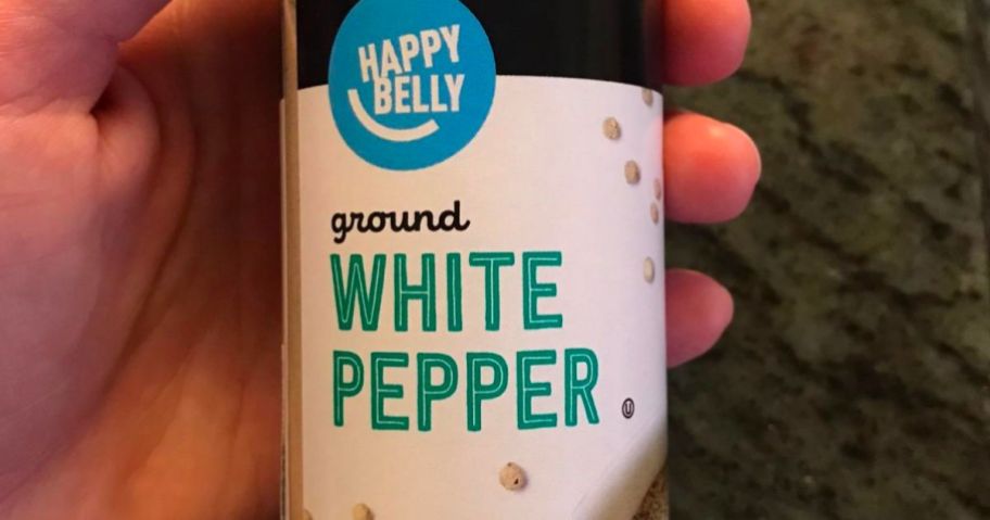 a mans hand holding a jar of Happy belly ground white pepper