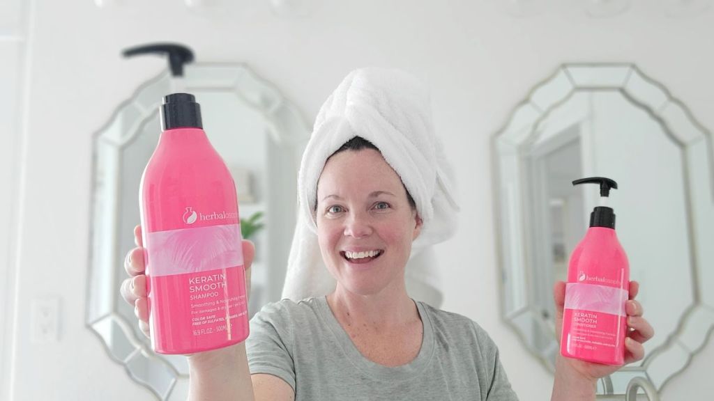 Woman holding pink shampoo and conditioner bottles