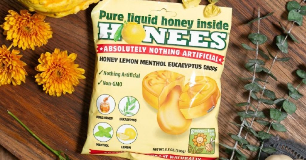 A bag of Honees cough drops on a wooden cou ntertop next to flowers and herbs