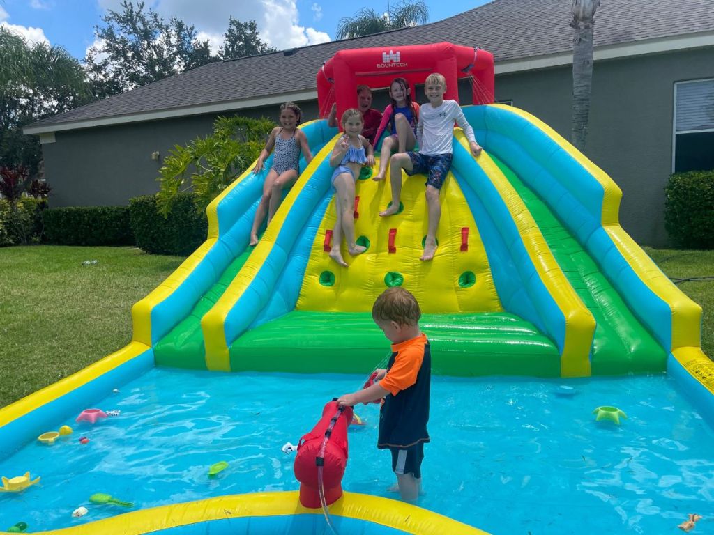 lots of kids playing in an inflatable water park in backyard