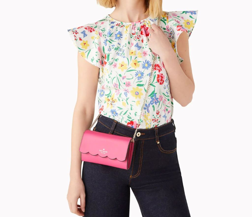 Woman in a floral shirt and black pants wearing a pink crossbody bag