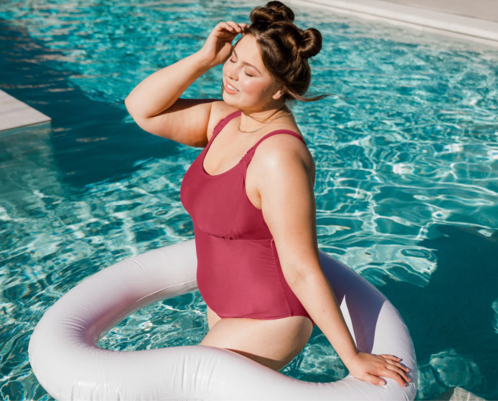 Woman in swimming pool modeling a Kindred Bravely plus size maternity swimsuit that can also be used for nursing
