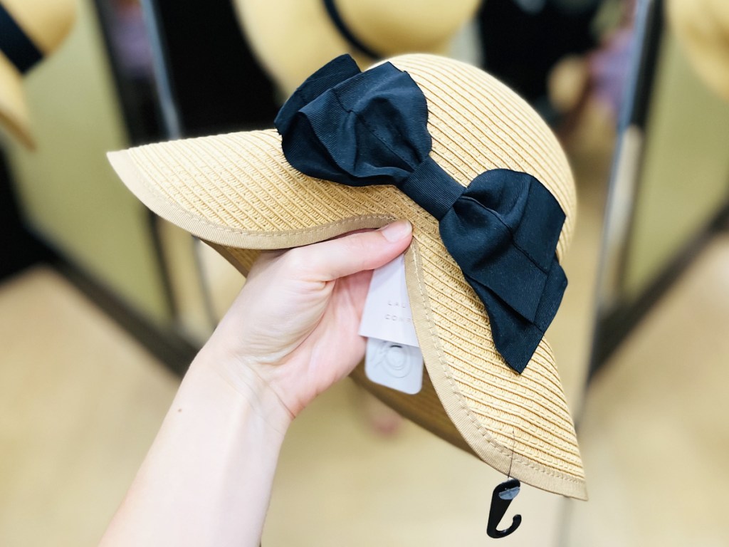 hand holding a straw hat with a black bow