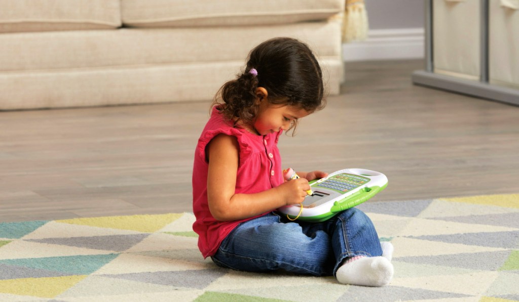 young girl playing with a LeapFrog Scribble and Write toy on the floor